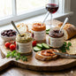 Hellenic Farms spreads on  jars on a wooden board with bread, olives, and tomatoes.